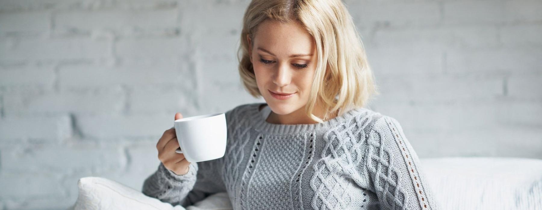 a woman sits on a couch with a cup of coffee and looks at her tablet